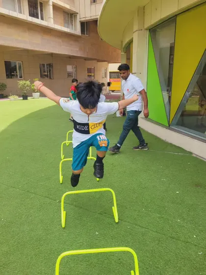 A young boy energetically jumps over hurdles during an outdoor fitness session. We use our green, open spaces to conduct dynamic drills that make exercise feel like play.