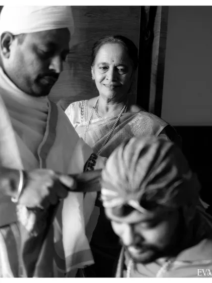 A poignant black and white photo of a mother looking on with love as her son participates in the wedding rituals.