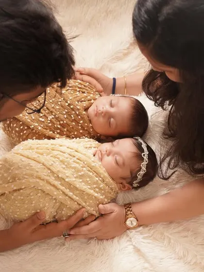 An intimate overhead shot of parents lovingly gazing at their newborn twins, who are swaddled peacefully together on a soft, fluffy blanket.