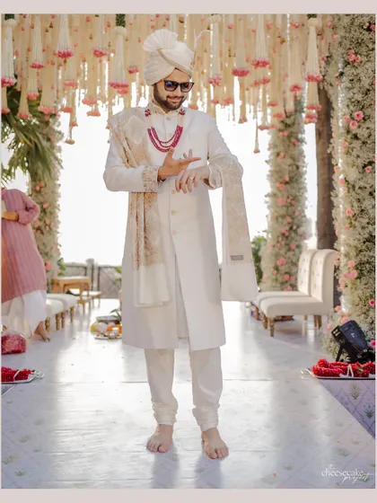 The groom awaits his bride, standing on a mirrored aisle that reflects the stunning floral decor. This setup highlights the grandeur of the entrance and the mandap.