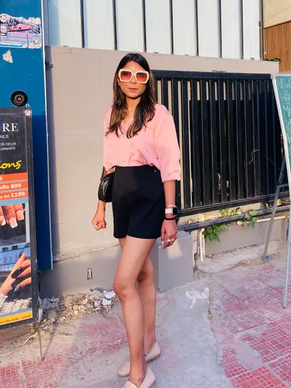 A summer look for a cafe outing in Delhi. A pink shirt paired with black shorts and statement sunglasses is a smart and comfortable choice for a hot day.