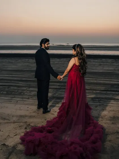 A romantic beach photoshoot at sunset. The deep red trail gown adds a touch of passion and elegance, flowing beautifully on the sand.
