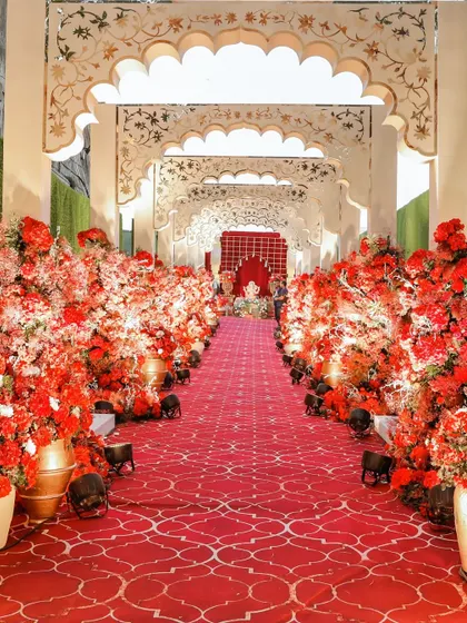 A royal walk through red blooms. The aisle is lined with a sea of red flowers and intricate arches, leading to a sacred space where new beginnings are blessed by Ganesha.