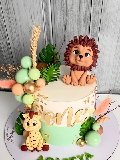 An adorable jungle-themed cake for a first birthday, featuring a hand-sculpted lion and giraffe, accented with pastel green and gold details, and dried botanicals.
