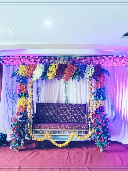 A colorful swing (jhula) decoration for a baby shower or Dohale Jevan ceremony. The swing is framed with multi-colored flowers, creating a joyful and festive look.