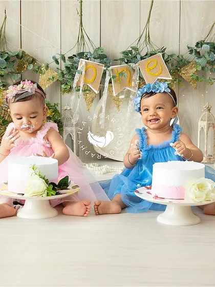 For this twin birthday shoot, each girl got her own beautiful cake. This setup with soft florals and a rustic backdrop creates a dreamy and celebratory atmosphere.