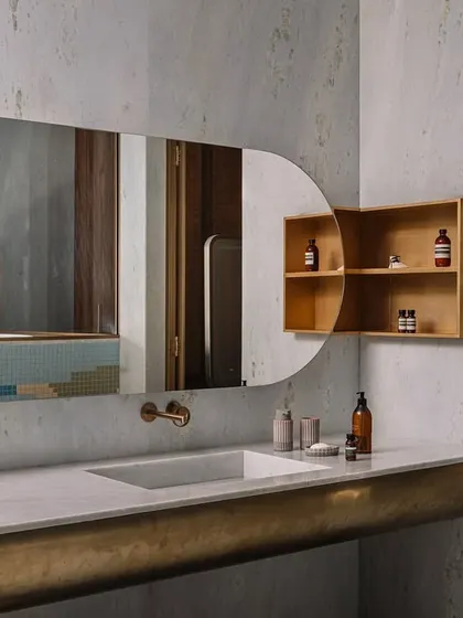 A bathroom in Rehethaan with a custom-curved vanity clad in brass, paired with a simple, integrated sink and a large, organically shaped mirror.