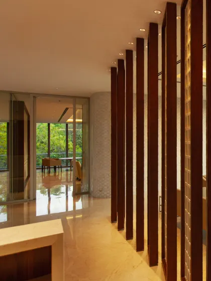A corridor at the Amara Raja campus defined by vertical wooden fins, which create a rhythmic play of light and shadow. The design guides movement while maintaining a sense of openness and connection to the adjacent green spaces.