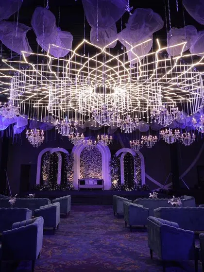 The same grand hall viewed from the entrance, showing the powerful first impression created by the custom lighting and stage design. The symmetrical arrangement of seating leads the eye towards the main stage, building anticipation for the event.