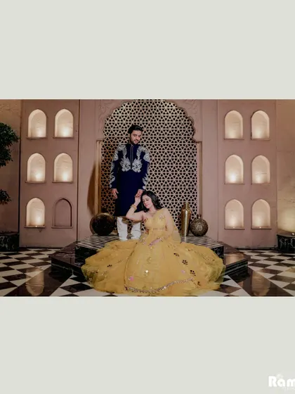 A majestic portrait set in a room with intricate jaali work and a checkered floor. The bride's yellow lehenga spreads out beautifully, creating a stunning composition full of royal vibes.