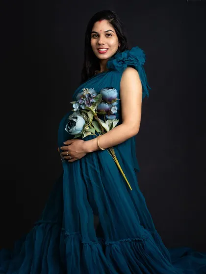 A beautiful smile that lights up the room. Dressed in a stunning teal gown and holding flowers, she looks absolutely radiant and full of joy.