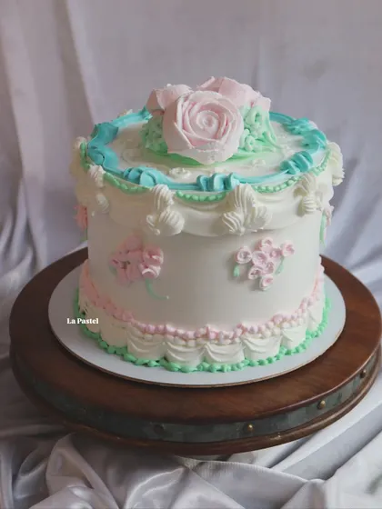 A vintage-style cake with delicate pastel piping in pink, blue, and green. The piped rose on top is the perfect finishing touch.