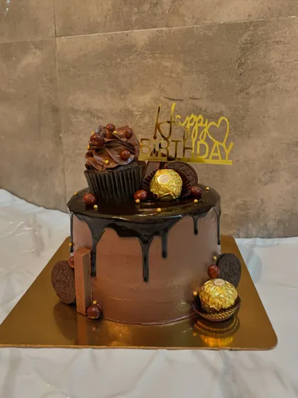 A rich chocolate drip cake decorated with Ferrero Rocher and a chocolate cupcake on top. It's a perfect birthday treat for any chocolate enthusiast.