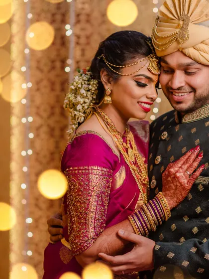 A close, romantic portrait of a South Indian couple. The bokeh from the background lights adds a magical, dreamy quality to the image.