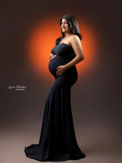 A full-length portrait in a classic black strapless gown. This is a timeless look that beautifully showcases the baby bump with elegance and grace.