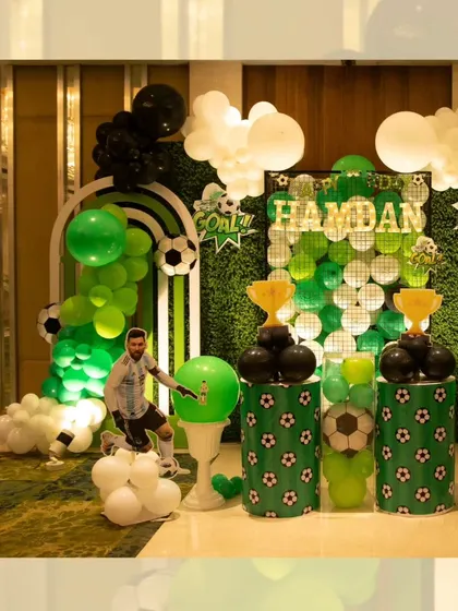 The main backdrop for a football-themed party, featuring a green balloon wall, a light-up name sign, and trophy props.