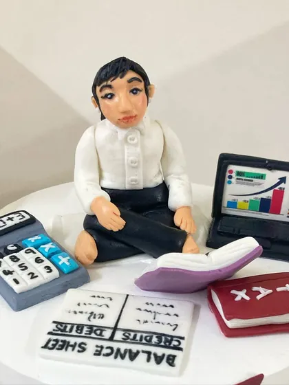 A close-up of the incredibly detailed, hand-sculpted fondant topper for the stock market cake, complete with a tiny laptop showing a rising chart.