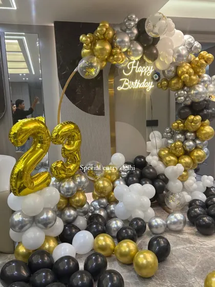 A lavish 23rd birthday setup with a golden ring frame. The decoration is filled with black, white, silver, and gold balloons, creating a luxurious feel.