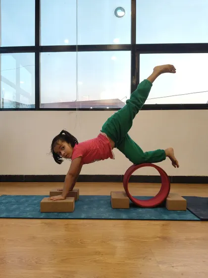This young yogi gets creative with blocks and a yoga wheel to practice a challenging balancing pose, improving her strength and coordination.