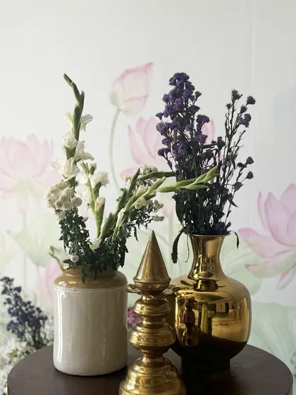 A beautiful floral arrangement in a traditional ceramic pot and a gleaming brass vase, set against a soft lotus-print wallpaper, blending heritage with elegance.