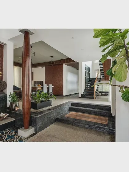 This image showcases the material palette, with a polished wooden pillar, textured laterite walls, and smooth black stone steps. The mix of materials creates a rich sensory experience as you move through the home.