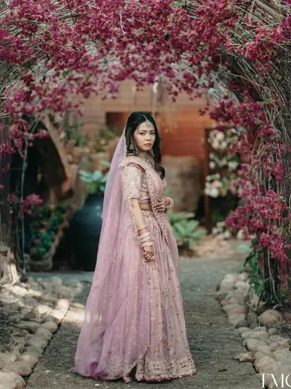 A fairytale moment. The bride stands under an arch of beautiful bougainvillea, her pastel lehenga perfectly complementing the floral surroundings in this stunning outdoor portrait.