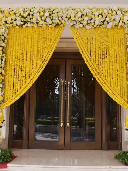 A beautiful entrance arch for a day wedding, featuring columns of yellow and white flowers and curtains made of marigold strings. This design is both traditional and incredibly cheerful.