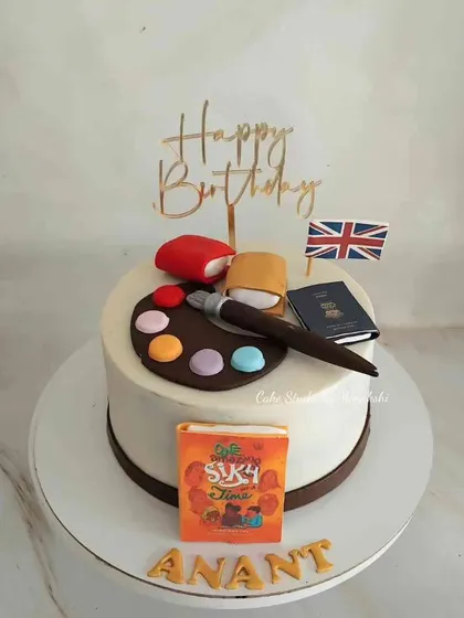A cake that tells the story of a book cover designer who loves to travel and paint. It features a passport, a paint palette, and a book.