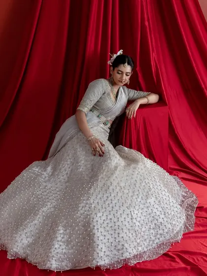 A graceful pose showcasing the expansive flare of the ivory lehenga skirt. The thousands of hand-embroidered details create a rich, textured surface that is both luxurious to the eye and to the touch.