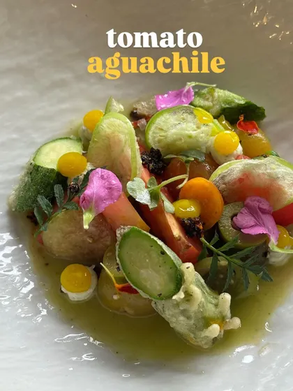 A close-up of the tomato aguachile, showcasing the variety of heirloom tomatoes, cucumbers, and edible flowers.