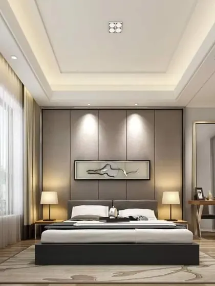 This bedroom design uses a layered false ceiling and spotlighting to create a warm and inviting ambiance. The room includes a small desk area by the window, making use of natural light.