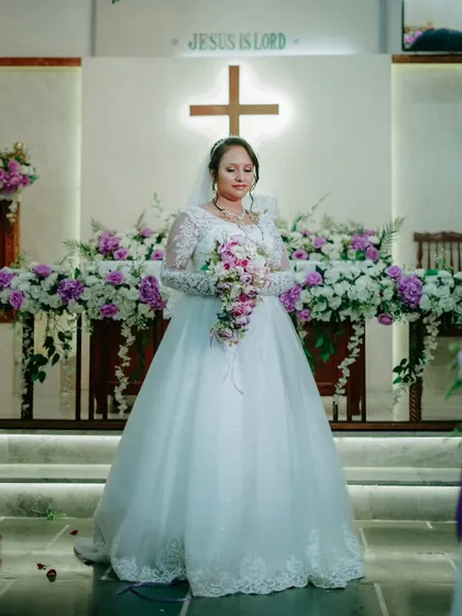 A full length portrait of the bride standing before the altar, which is beautifully decorated with flowers.
