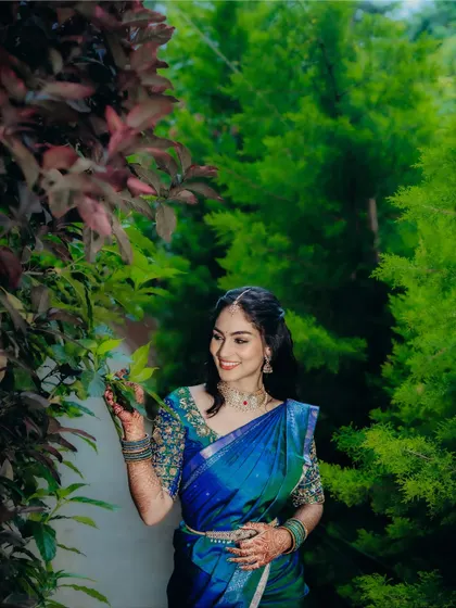 Surrounded by lush greenery, her vibrant blue saree and radiant makeup create a stunning contrast. This is a perfect example of a daytime engagement look.