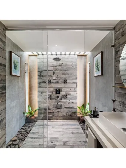 This bathroom in "The Far Site House" uses wood-finish tiles and river pebbles to create a rustic, nature-inspired look. The walk-in shower with a rain shower head adds a touch of modern luxury.