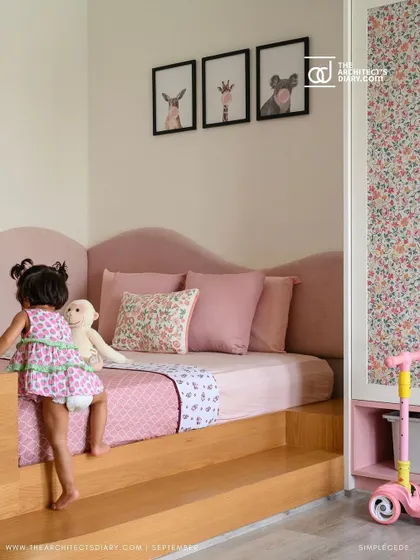 A little girl enjoys her new room in the 'Cover me in Sunshine' project. The platform bed with a wavy, upholstered headboard is safe and inviting, creating a perfect space for a toddler.