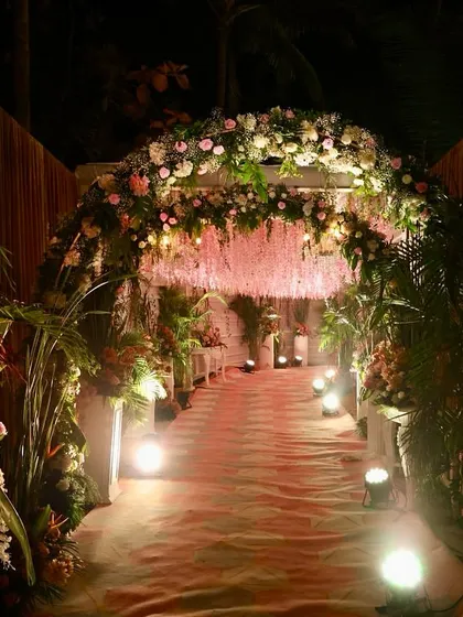 We create enchanting pathways for your guests. This entrance features a lush floral arch and a ceiling of hanging pink blossoms, warmly lit to welcome everyone into the celebration.