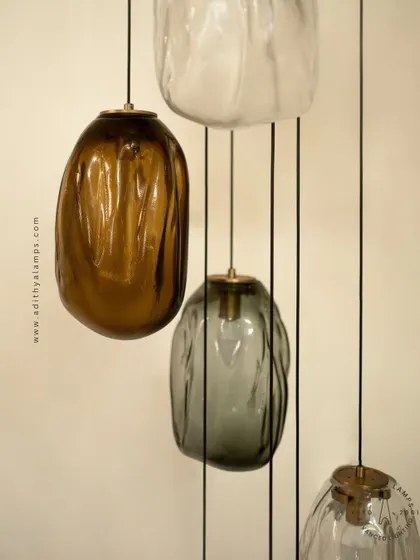 This cascading installation features pendants made of organic, free-form glass in smoked and amber tones. The textured, irregular shapes create a beautiful, water-like effect, perfect for adding a sense of calm and artistry to a room.