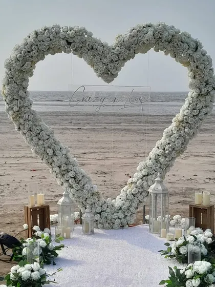 A breathtaking beach proposal setup in Mumbai, featuring a custom heart-shaped arch of white flowers and a 'Crazy in Love' neon sign. We designed this to create a truly magical and picture-perfect moment for the couple.