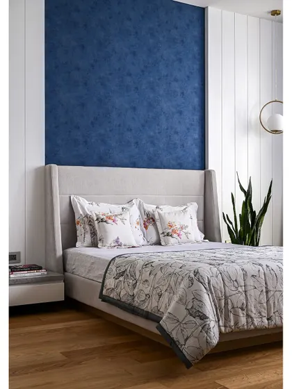 The guest bedroom has a cozy, inviting vibe, with a wingback upholstered bed set against a deep blue textured wallpaper panel.