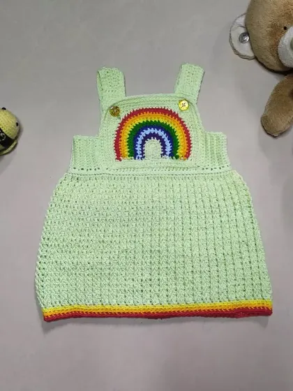 The Lucky Rainbow Dress is such a happy piece. Made with a soft green cotton yarn and a vibrant rainbow applique, this overall-style dress is both comfortable for playtime and cute enough for any special day.