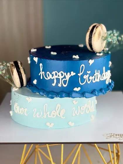 This off-centered sliding cake brings a playful twist to birthday celebrations. The two blue tiers are stacked unconventionally and decorated with macarons and sweet messages.