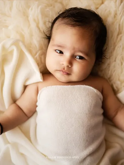 A simple and beautiful portrait of a newborn wrapped in a soft white cloth, lying on a fluffy blanket. This shot highlights their delicate features.