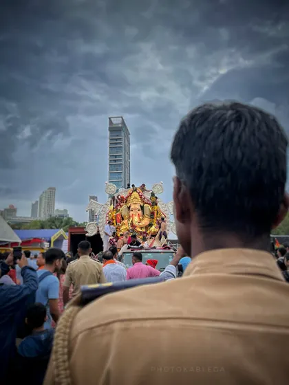 A poignant shot from behind a police officer watching over the GSB Seva Mandal Visarjan. It captures a quiet moment of duty and devotion amidst the grand scale of the event.
