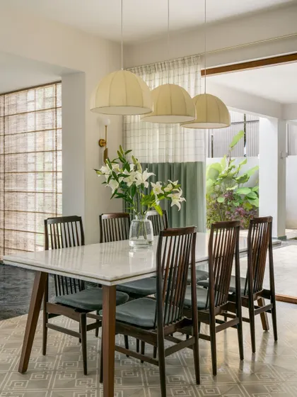 The dining area is situated next to a courtyard, with large windows that let in natural light. The material palette is a mix of patterned heritage floor tiles and a modern marble-topped dining table.