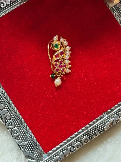 A peacock-inspired nath with red and green stones and a pearl drop.