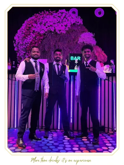 Our bartending crew posing in front of a vibrant, floral-topped bar. We are always ready to serve with style and a positive attitude.