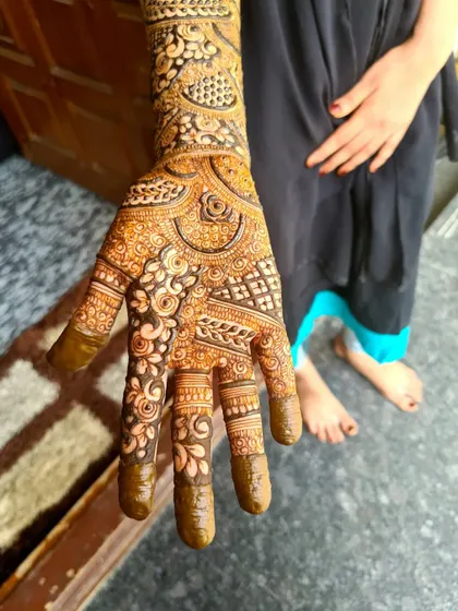 A detailed view of a bride's palm and forearm, showing a combination of floral work, leaf patterns, and checkerboard fillers.