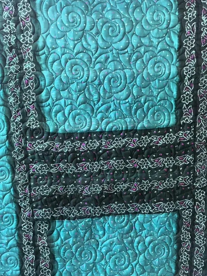 A detailed view of the swirling rose longarm quilting on a teal saree quilt, adding another layer of artistry to the piece.