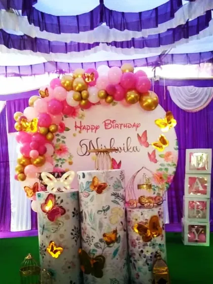 A simple and sweet butterfly theme for baby Nishvika's birthday. This outdoor setup includes a round backdrop with butterfly details and a pink and gold balloon garland.