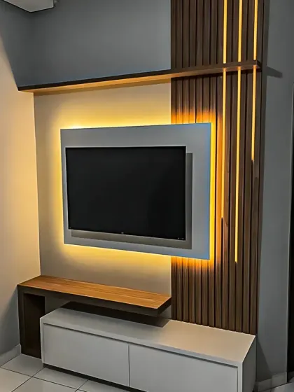 A modern TV unit design where ambient backlighting makes the screen appear to float. The vertical wood slats add texture and contrast to the minimalist white console.
